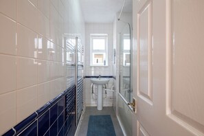 A narrow bathroom with white tiles, a sink, and a shower area. - Spacious 3BDR Flat Near the Tower of London (Greater London)