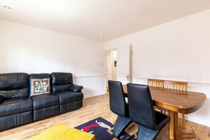 Ein Wohnzimmer mit einer schwarzen Ledersofa, einem Holzesstisch mit Stühlen und einem gemusterten Teppich.