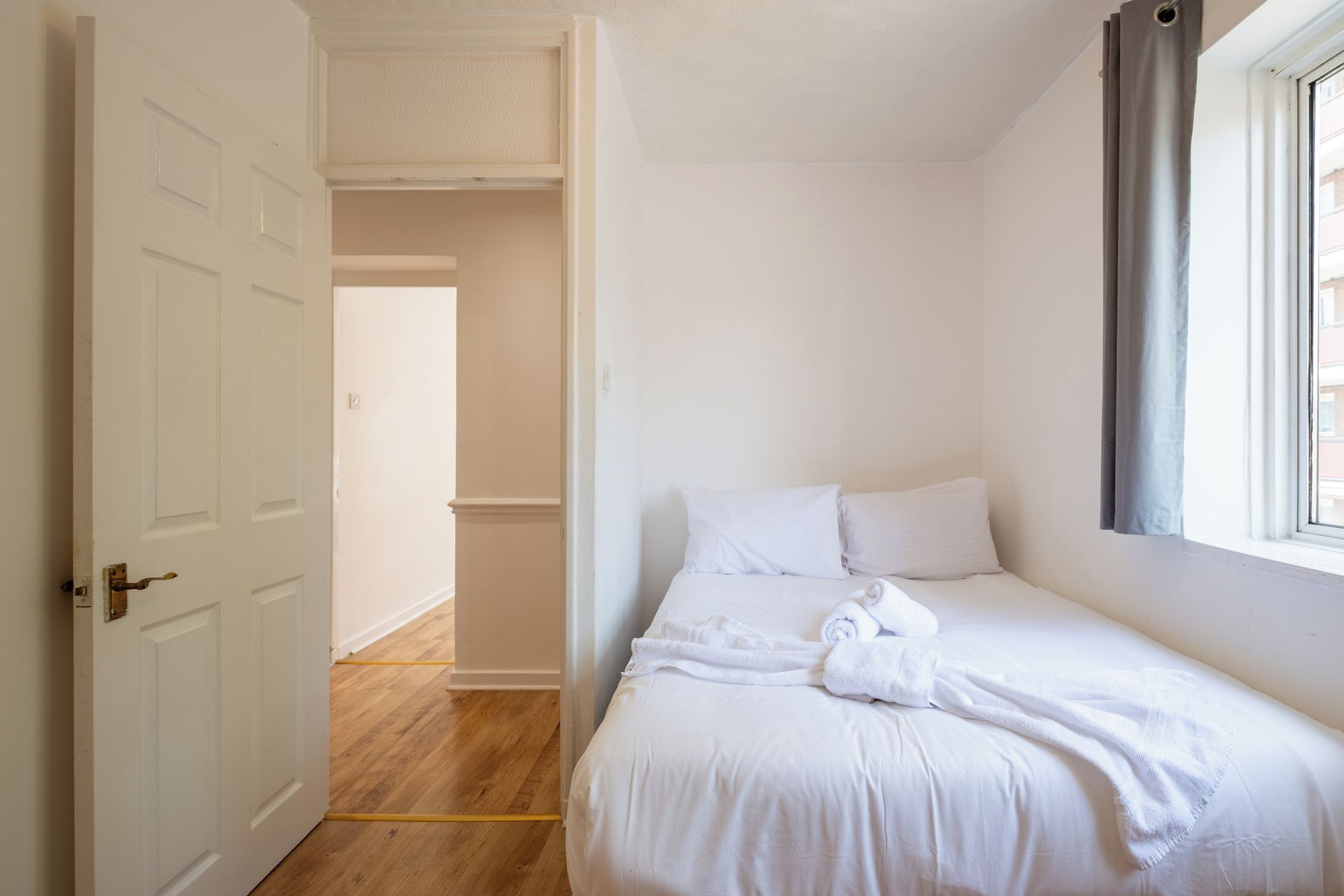 Une chambre à coucher avec un lit, une fenêtre avec des rideaux et une porte donnant sur une autre pièce.