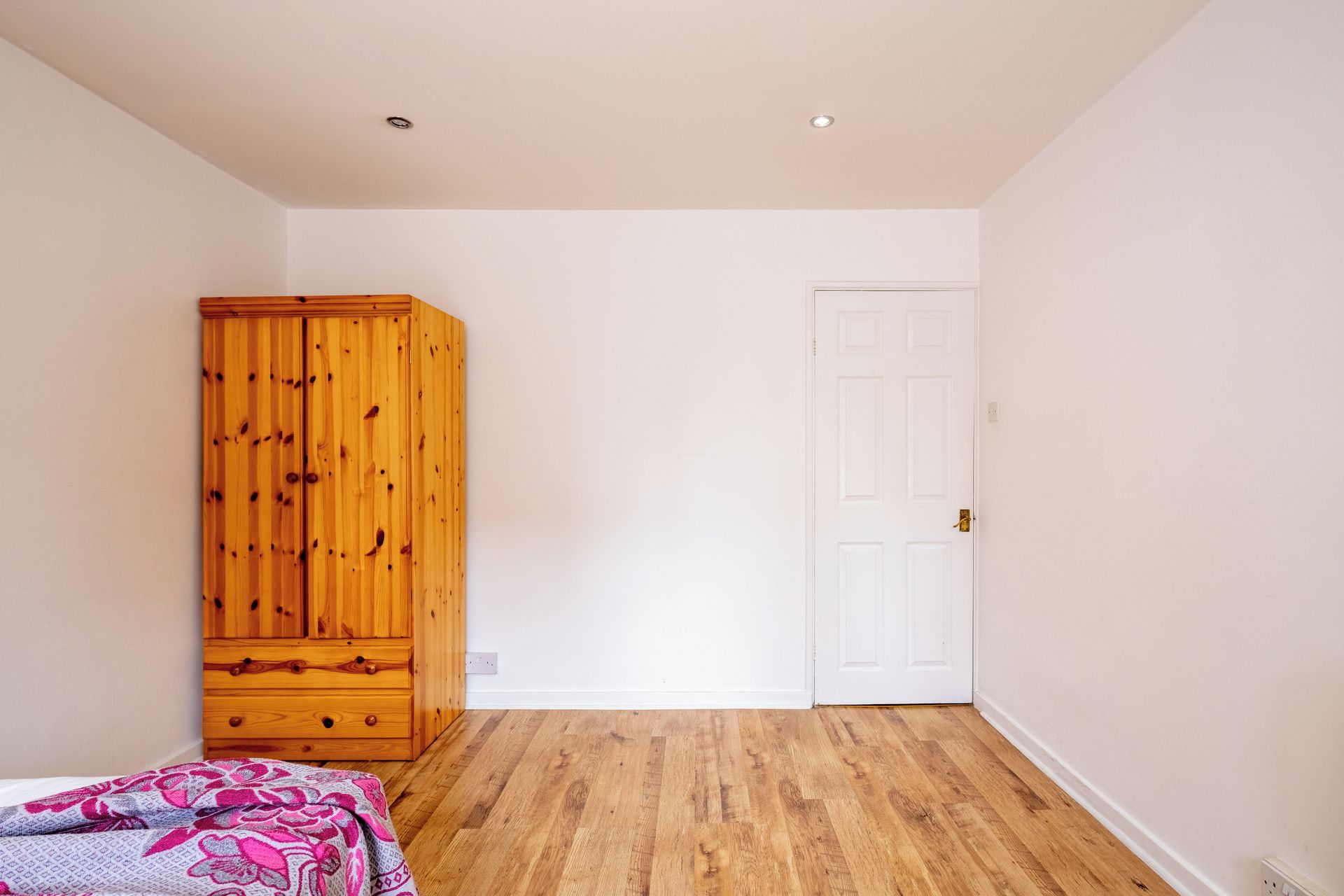 Een slaapkamer met een houten garderobe, een witte deur en een bed met een decoratief sprei.