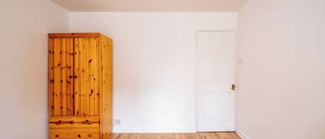 Een slaapkamer met een houten garderobe, een witte deur en een bed met een decoratief sprei.