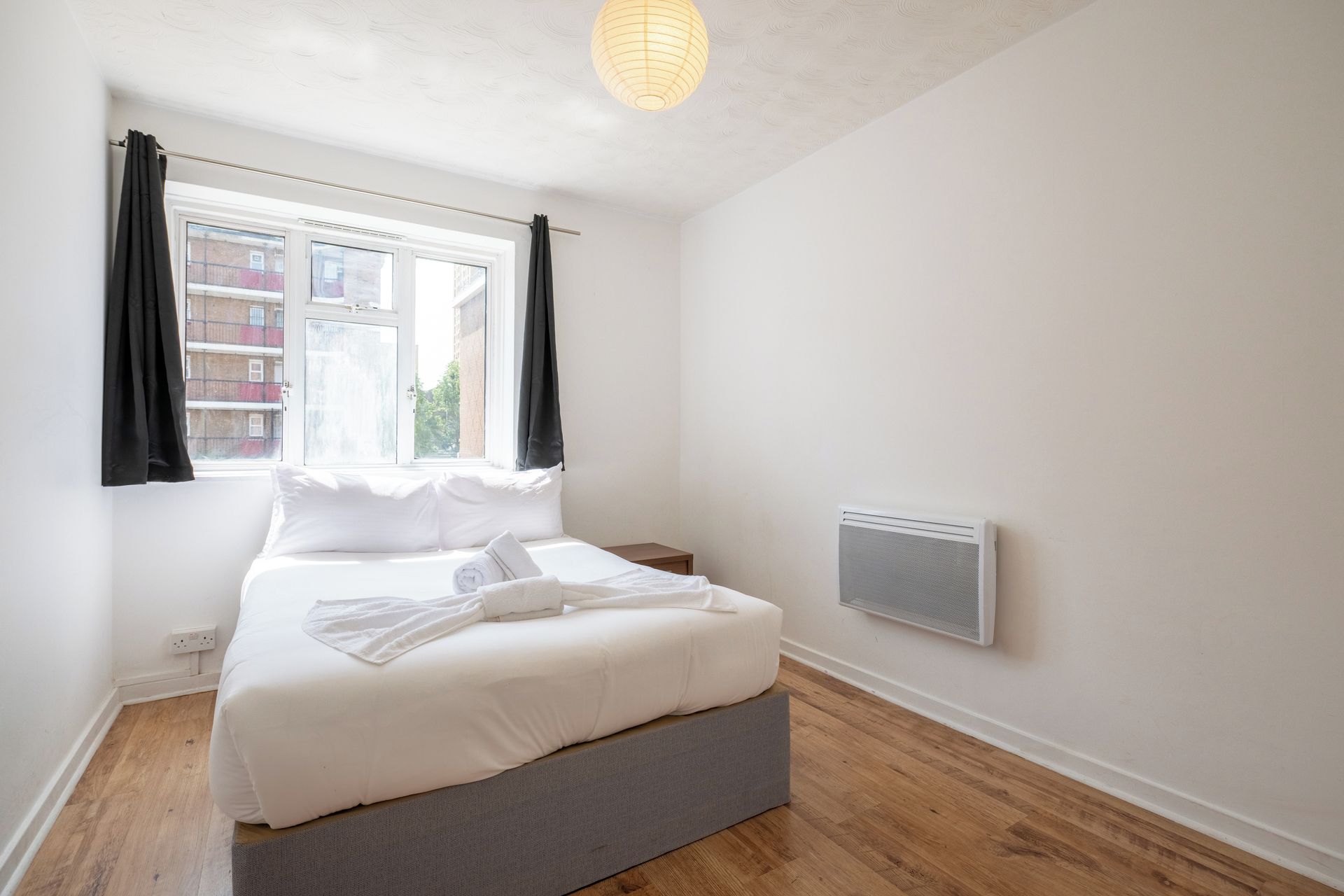 A bedroom with a bed, a window with curtains, a radiator, and a wooden floor.