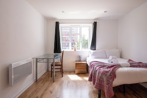 A bedroom with a bed, a bedside table, a chair, a desk, and a window with curtains. - Spacious 3BDR Flat Near the Tower of London (Greater London)