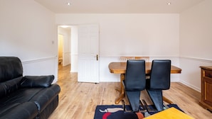 Een moderne woonkamer met een zwarte leren bank, een houten eettafel met twee stoelen en een houten kast.