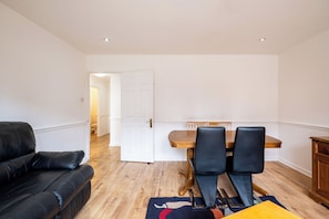 A modern living room with a black leather sofa, a wooden dining table with two chairs, and a wooden cabinet. - Spacious 3BDR Flat Near the Tower of London (Greater London)