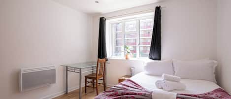 A hotel room with a bed, a desk, and a window with curtains.