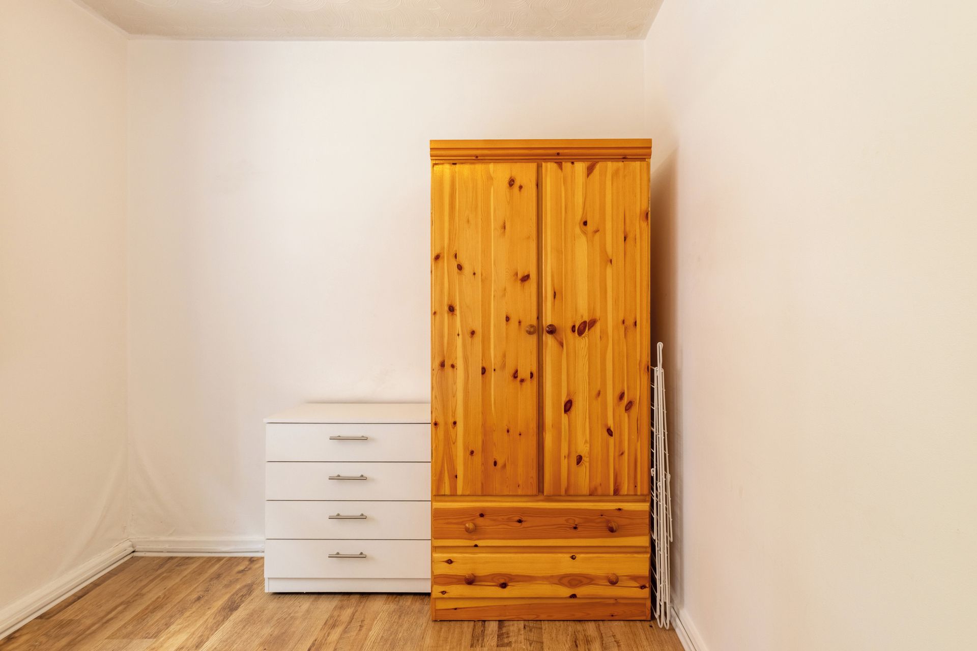 A room with a wooden wardrobe, a white chest of drawers, and a radiator.