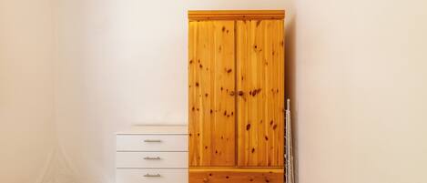 A room with a wooden wardrobe, a white chest of drawers, and a radiator.