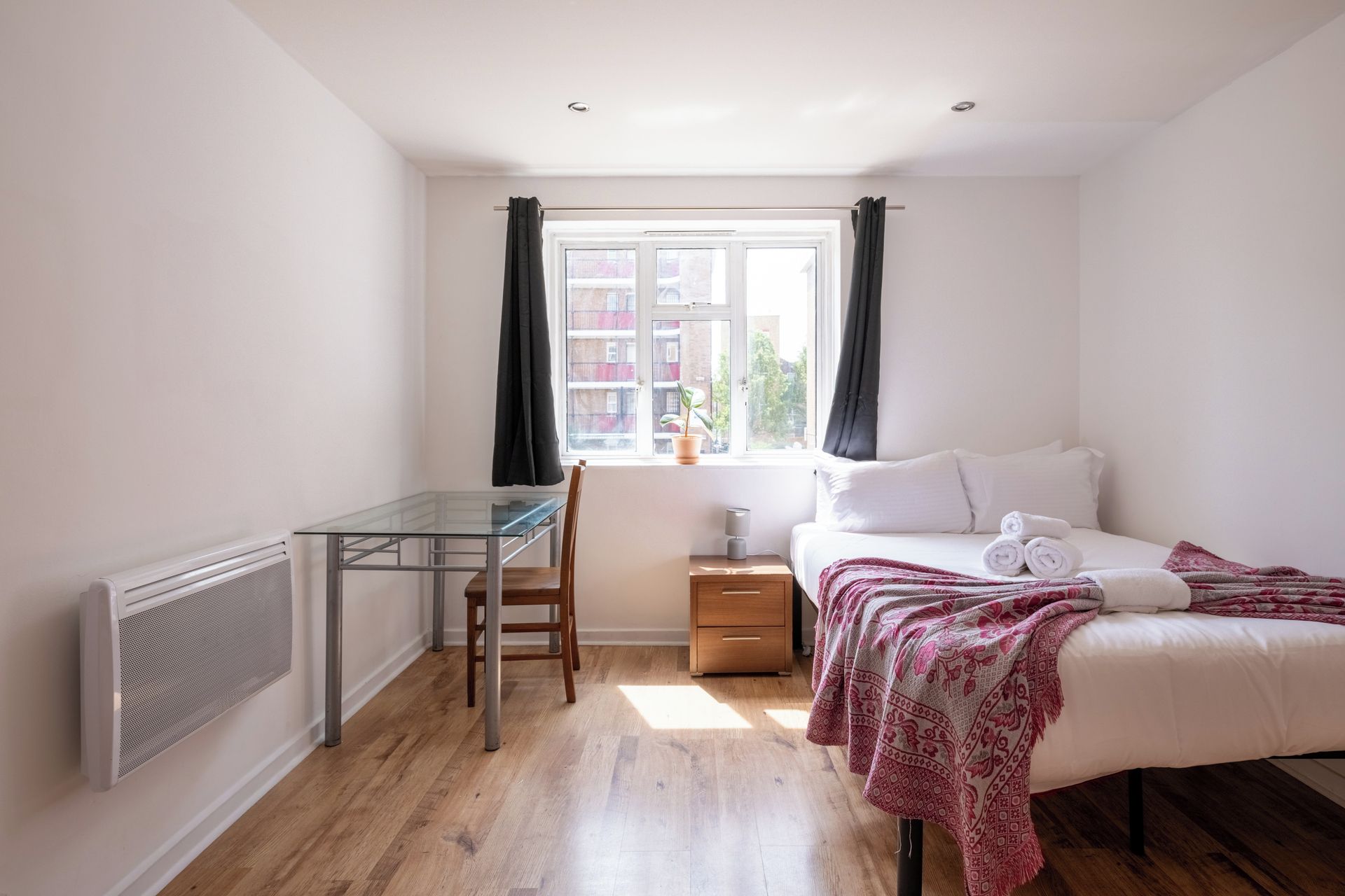A bedroom with a bed, a bedside table, a chair, a desk, and a window with curtains.