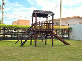 Uma estrutura de madeira para brincar com telhado e escorregas em um gramado.
