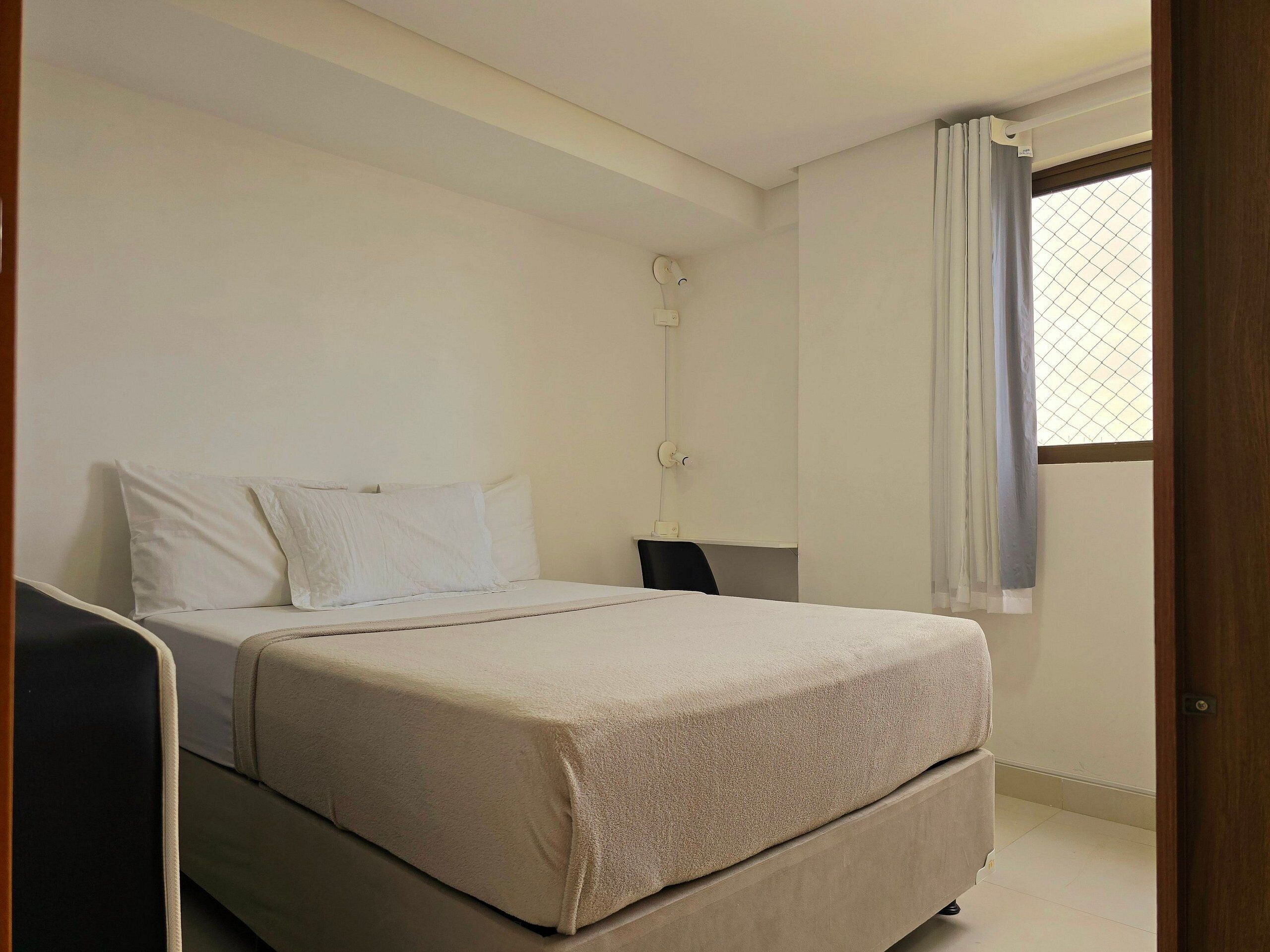 Un dormitorio con cama, mesita de noche, lámpara y ventana con cortinas.
