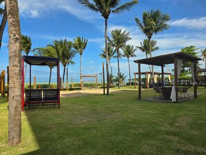 A beachside park with seating areas, a volleyball net, and palm trees. - Amaranth By Hosppedar (Cabedelo)