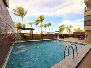 A swimming pool with a clear blue water, surrounded by a fence, and palm trees in the background.