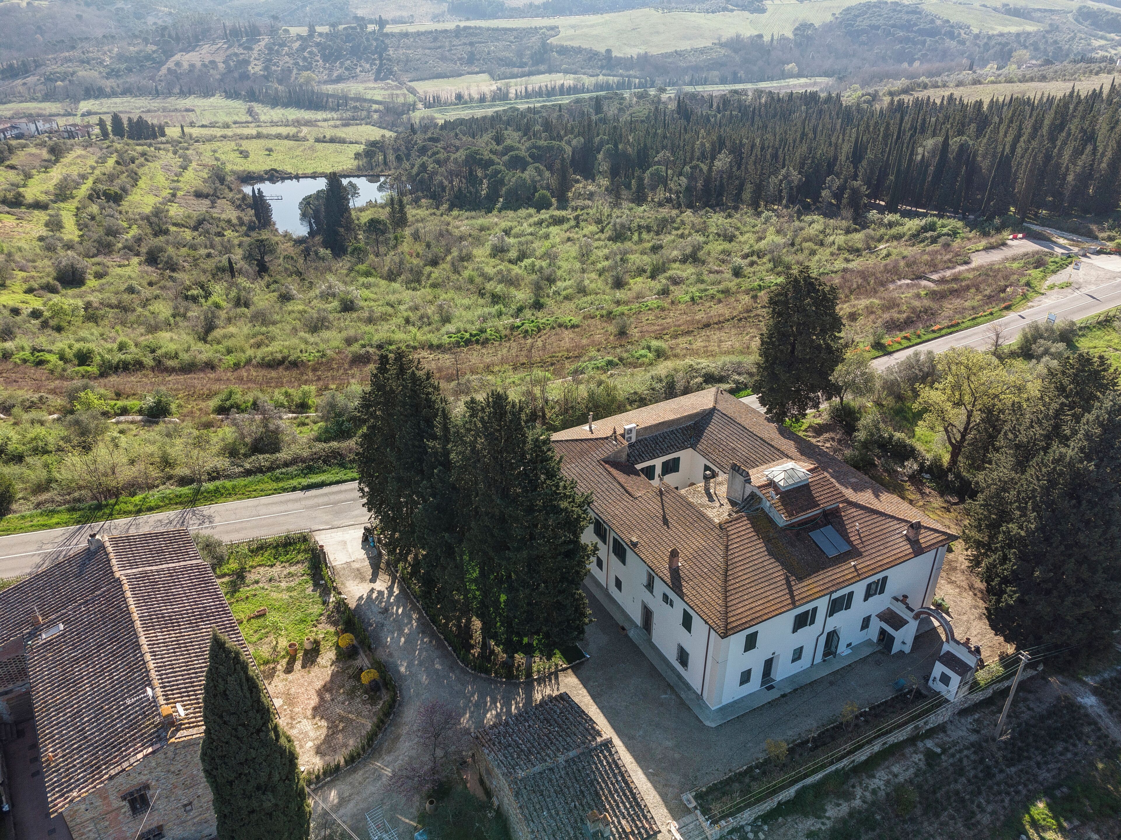 A large building with multiple windows and a sloped roof, surrounded by greenery and a small body of water.
