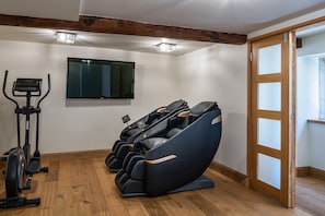 A room with a massage chair, a treadmill, and a television on the wall.