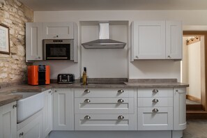A kitchen with white cabinetry, a built-in oven, a range hood, and a countertop with a toaster and a bottle.