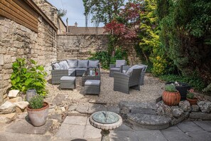 An outdoor seating area with wicker furniture, a stone wall, and potted plants.