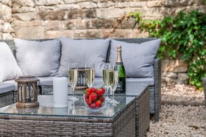 A wicker table with glasses of champagne, a candle, and a bowl of strawberries.