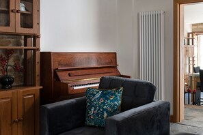 A room with a wooden piano, a dark armchair with a floral pillow, and a radiator.