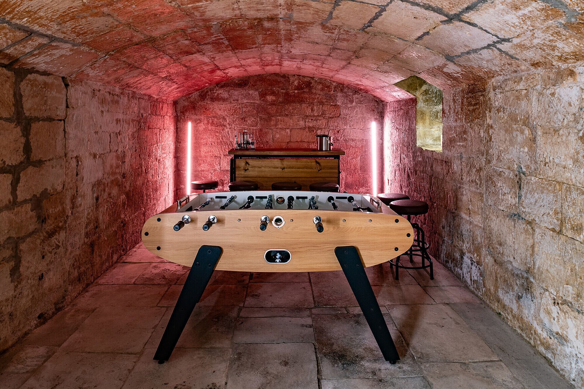 A room with a wooden foosball table, a wooden cabinet, and a red brick wall.