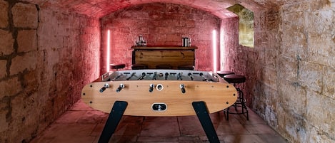 A room with a wooden foosball table, a wooden cabinet, and a red brick wall.