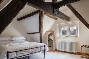 A bedroom with a sloped ceiling, a bed, a mirror, a radiator, and a window.
