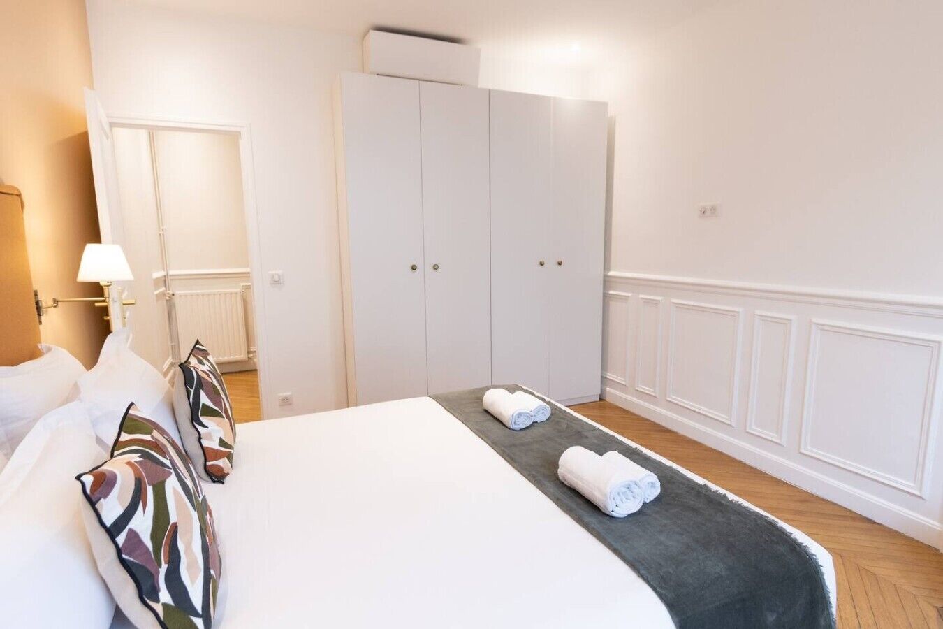 A hotel room with a bed, a wardrobe, a lamp, and a radiator.