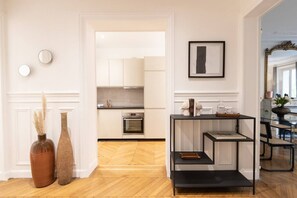 A modern kitchen with white cabinetry, a black countertop, and a built-in oven. There is a black metal shelf unit with decorative items on top. - A2-8 people-4 bedrooms-Wagram-AC-Paris 8 (Paris)