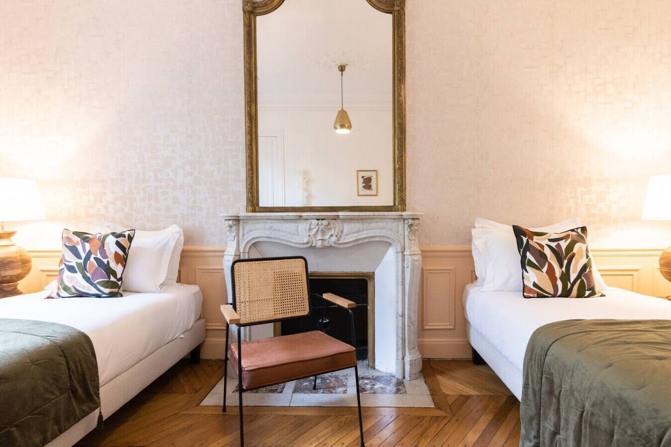 Habitación de hotel con dos camas, chimenea, espejo y una silla.