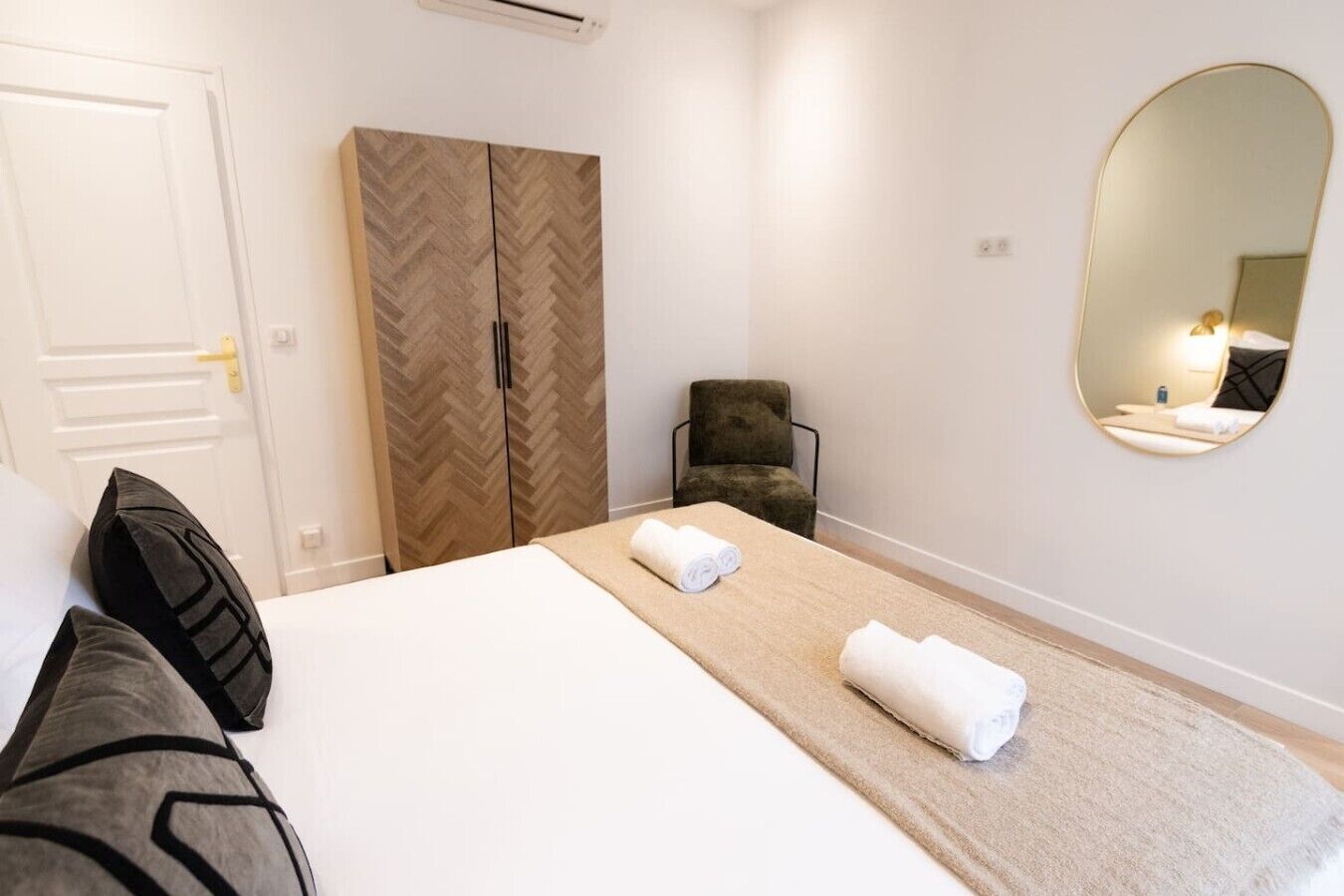 A hotel room with a bed, a wardrobe, a chair, a round mirror, and a towel on the bed.