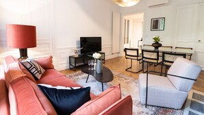 A living room with a sofa, a coffee table, a TV, and a dining area with chairs and a table. - A2-8 people-4 bedrooms-Wagram-AC-Paris 8 (Paris)