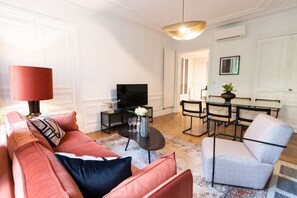 A living room with a sofa, a coffee table, a TV, and a dining area with chairs and a table. - A2-8 people-4 bedrooms-Wagram-AC-Paris 8 (Paris)