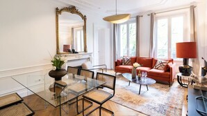 A room with a glass dining table, a red sofa, and a large mirror. - A2-8 people-4 bedrooms-Wagram-AC-Paris 8 (Paris)