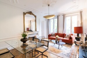 A room with a glass dining table, a red sofa, and a large mirror. - A2-8 people-4 bedrooms-Wagram-AC-Paris 8 (Paris)
