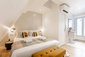 Ein modernes Schlafzimmer mit einem großen Bett, einem Nachttisch mit Lampe, einer Bank und Blick ins Bad.