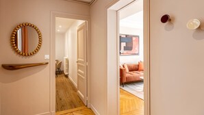 A hallway with a wooden floor, a mirror with a golden frame, and a door leading to a room with a sofa and a painting. - B2G. 6 people—Champs-Élysées—Wagram—Arc de Triomphe—AC (Paris)