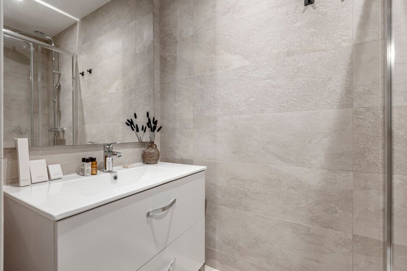A modern bathroom with a white vanity, a glass shower enclosure, and a marble wall.