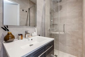Uma casa de banho moderna com uma grande pia branca, um chuveiro com divisória de vidro e um espelho sobre a pia.