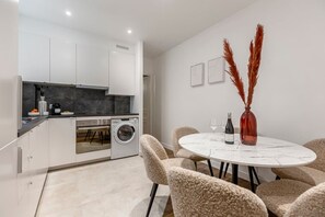 A modern kitchen with a washing machine, a dining area with a round table and chairs, and a vase with pampas grass. - B2G. 6 people—Champs-Élysées—Wagram—Arc de Triomphe—AC (Paris)