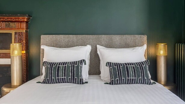 A bed with white bedding and two pillows, one plain white and one striped, against a green wall. - B2G. 6 people—Champs-Élysées—Wagram—Arc de Triomphe—AC (Paris)