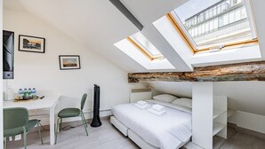 Et værelse med køjeseng, et skrivebord med stol, en guitar og et ovenlys.