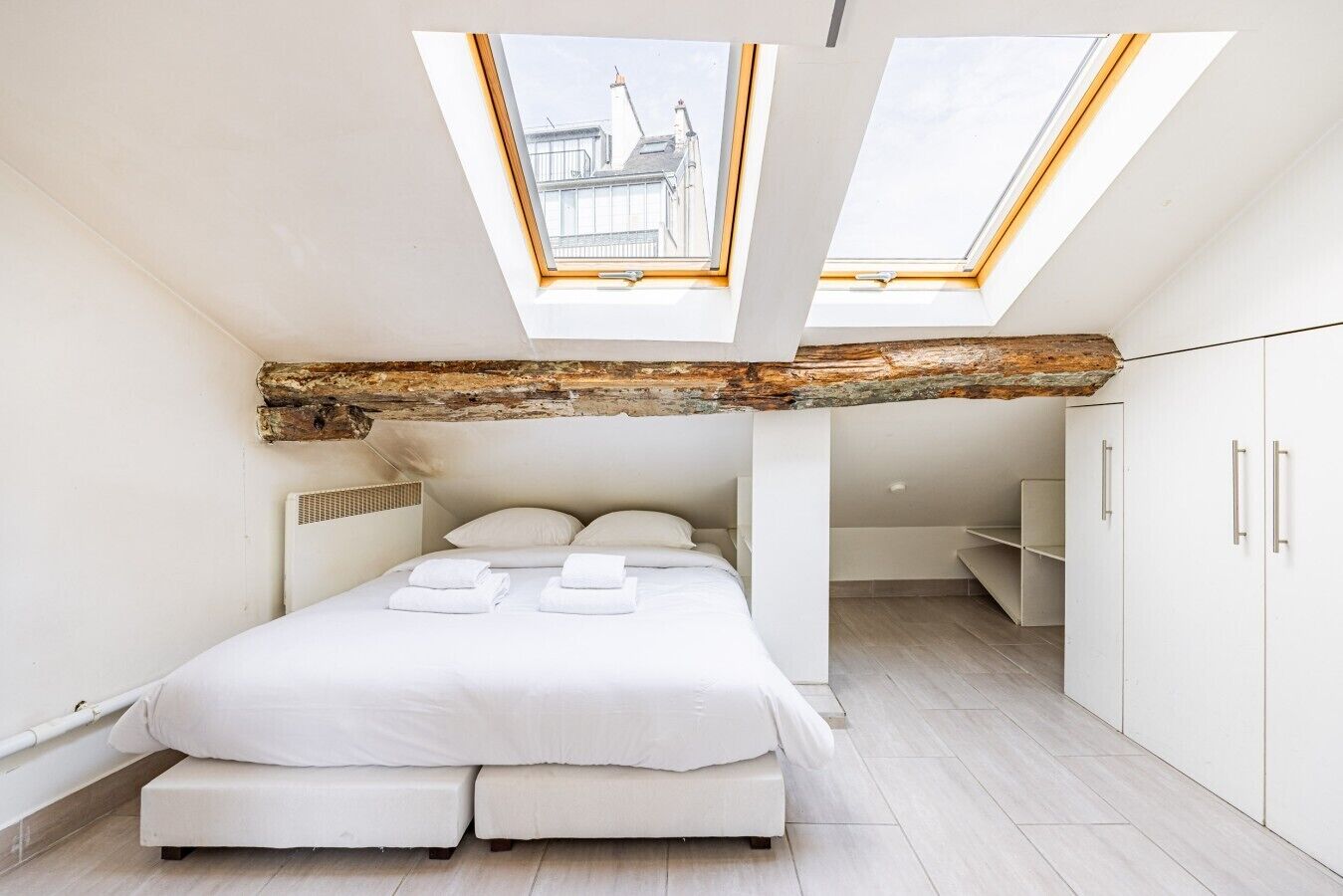 A modern bedroom with a skylight, a bed with pillows, and a wooden beam ceiling.