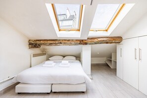 A modern bedroom with a skylight, a bed with pillows, and a wooden beam ceiling. - Palais Royal – Louvre Museum – Central Studio (Paris)