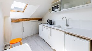 Et kompakt køkken med ovenlys, hvide skabe, en vask og et køleskab.