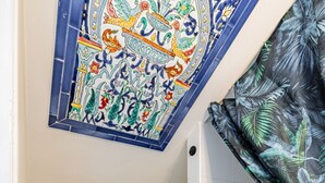 Et badeværelse med et hvidt toilet, en skraldespand, et bruseområde og et dekorativt fliseloft.