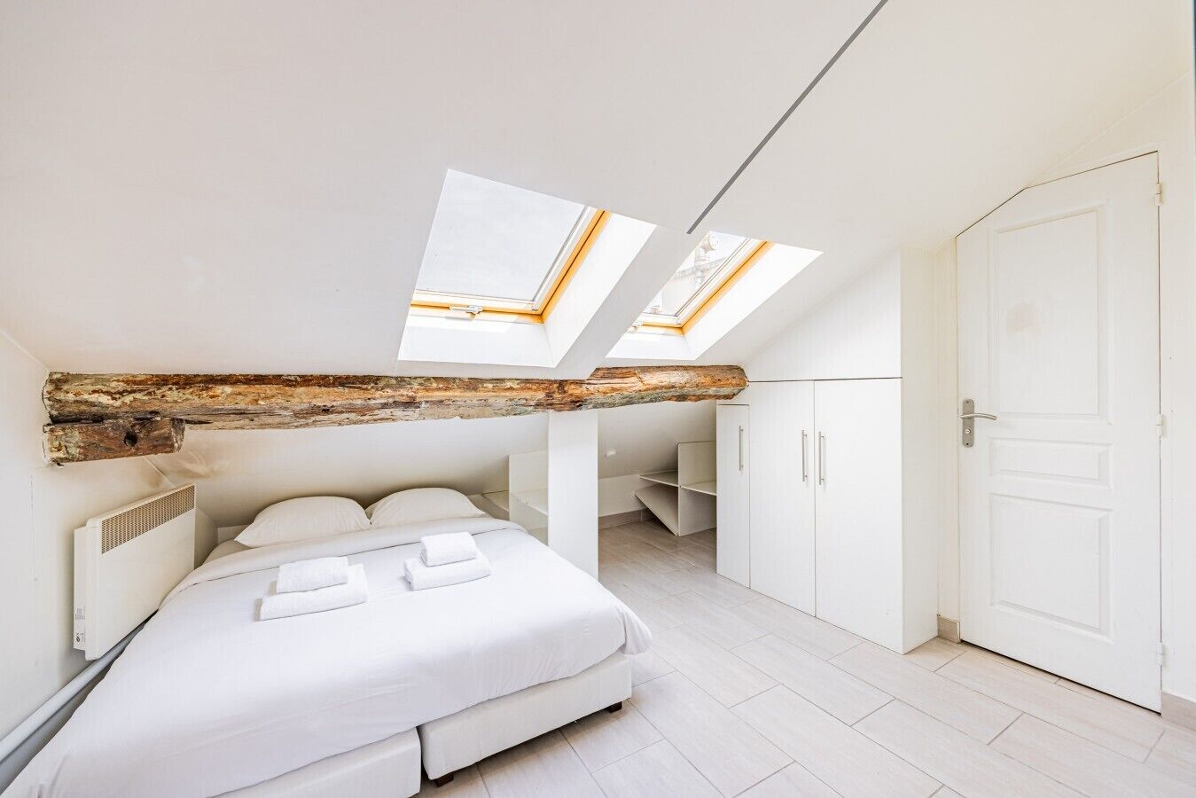 A bedroom with a skylight, a bed, a wardrobe, and a door.