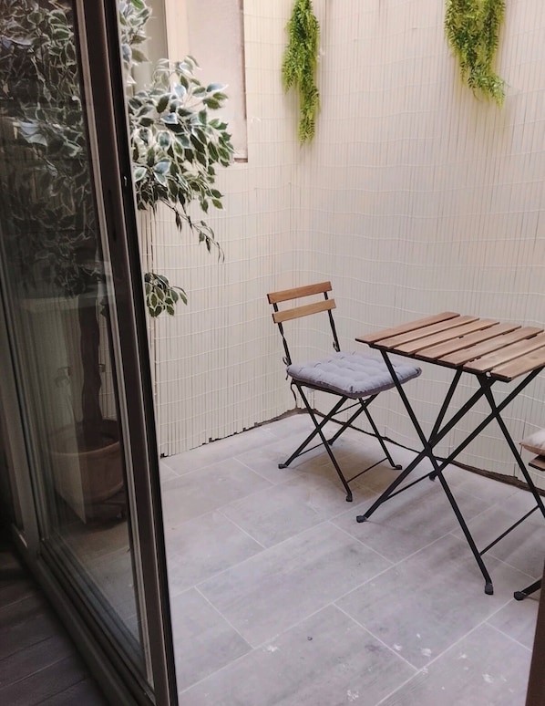 A small patio area with a wooden table and a chair, a potted plant, and a wall-mounted plant.