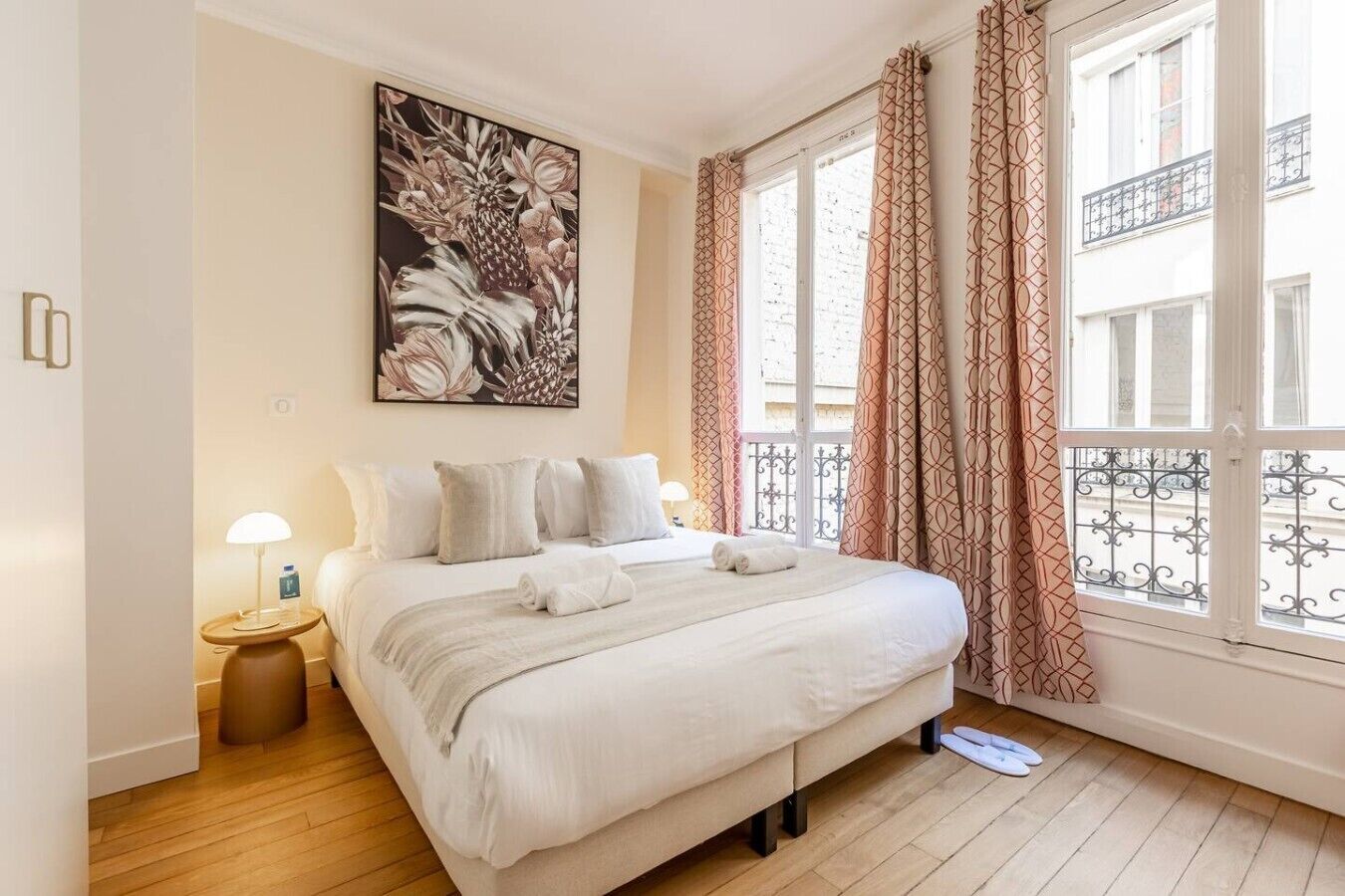 A hotel room with a bed, a nightstand, a lamp, a painting, and a window with curtains.