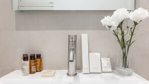 Un lavabo de salle de bain avec des articles de toilette, un miroir et un vase de fleurs.