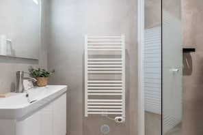 Ein Badezimmer mit einem weißen Waschbecken, einem modernen Wasserhahn, einer Topfpflanze und einem weißen Handtuchhalter.